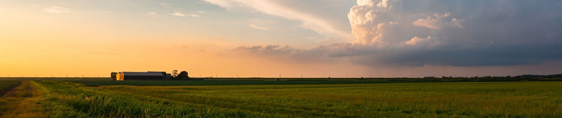 Een boerderij in de verte en onweerswolk op het Nederlandse platteland tijdens zonsondergang